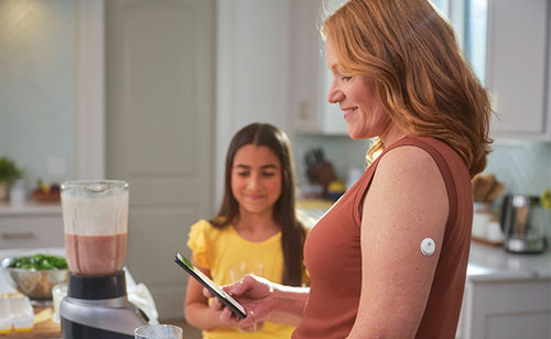 Frau mit einem Smartphone in der Hand. Am Oberarm trägt sie einen Sensor.
