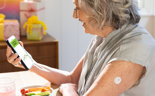 Frau mit einem Smartphone in der Hand. Am Oberarm trägt sie einen Sensor.