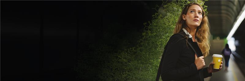 Eine junge Frau mit Kaffeebecher in der Hand und besorgtem Blick an einem Bahnsteig. Neben ihr bauen sich Ketonverbingungen in bedrohlicher Weise auf.