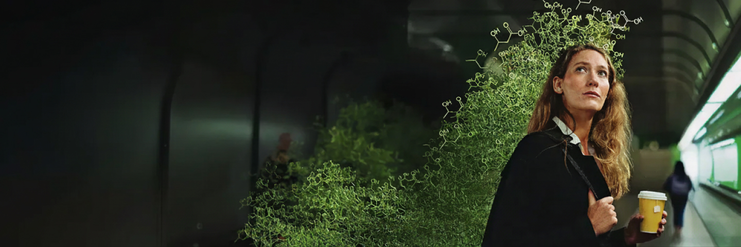 Eine junge Frau mit Kaffeebecher in der Hand und besorgtem Blick an einem Bahnsteig. Neben ihr bauen sich Ketonverbingungen in bedrohlicher Weise auf.