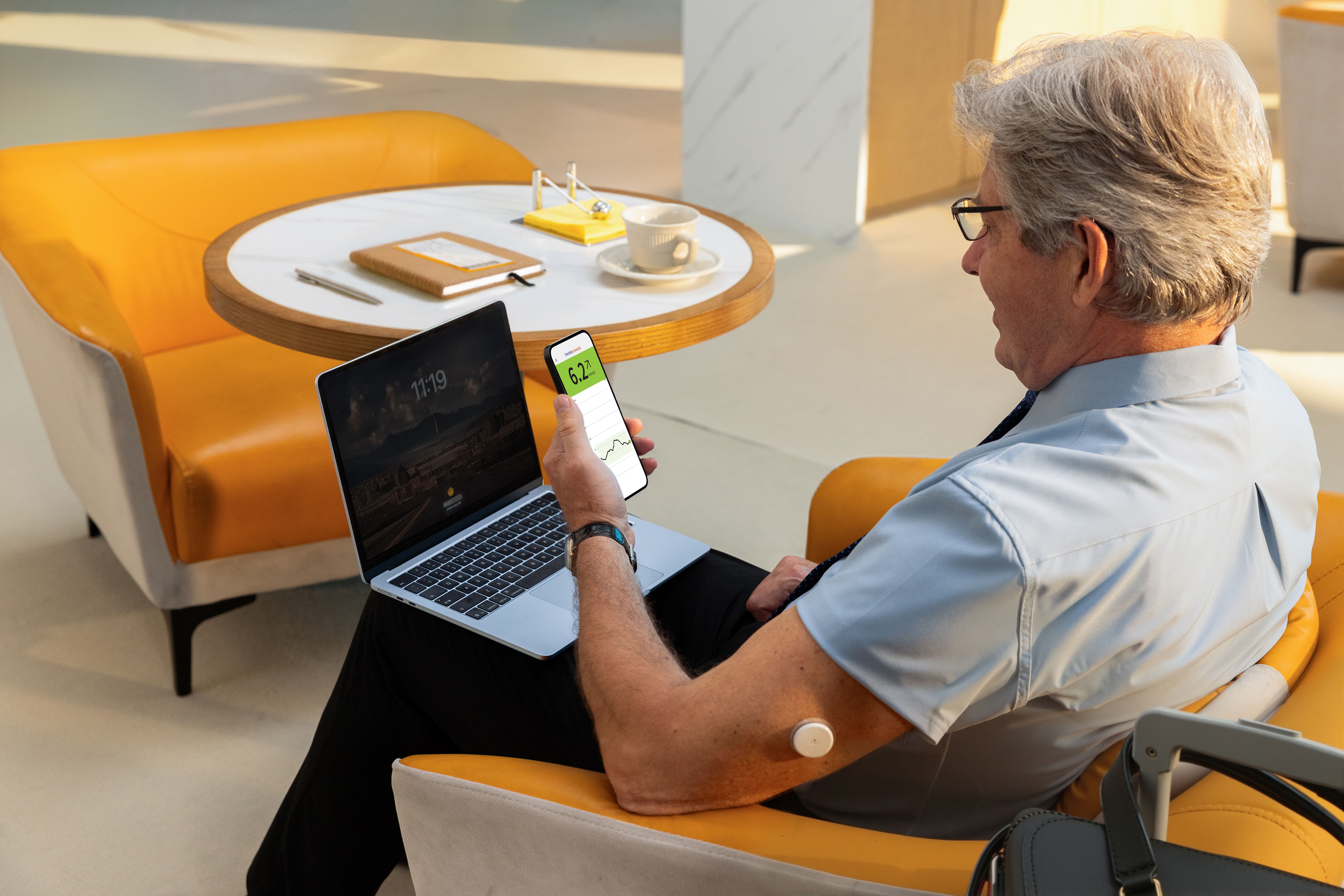 A Libre 2 Plus sensor user checking glucose readings on his phone and sitting on a chair