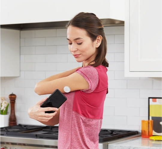 FreeStyle Libre System user scanning the sensor on her arm with her phone in the kitchen. 