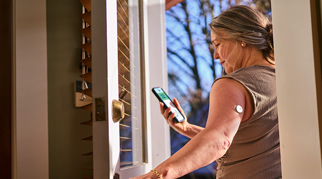 Woman with FreeStyle Libre 2 Plus sensor looking at her phone