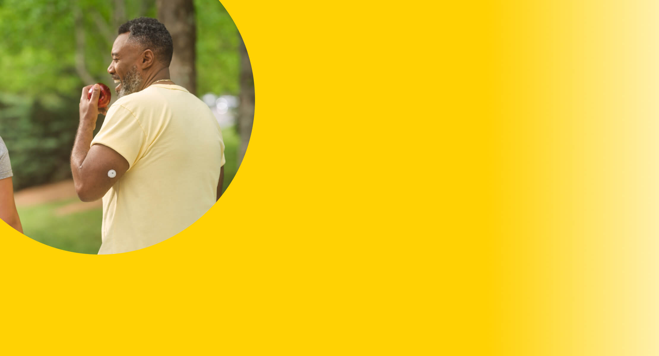 A man walking outdoors and eating an apple, he has a visible sensor on his arm 