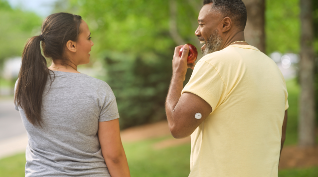 A man walking outdoors and eating an apple, he has a visible sensor on his arm 
