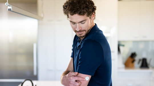 A FreeStyle Libre System user looking down and touching the sensor on the back of his upper arm.