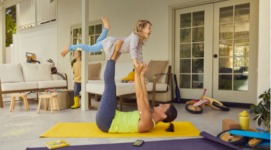 A FreeStyle Libre System user doing yoga. She is holding a child above her head using her hands and feet.