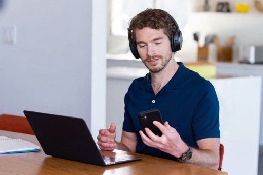 Ein Mann sitzt an einem Schreibtisch mit einem Laptop und einem Smartphone.