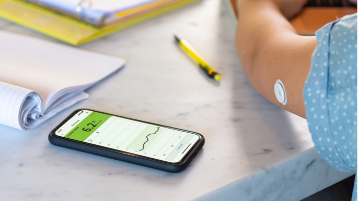 A FreeStyle Libre System user's arm showing their sensor alongside the FreeStyle LibreLink app shown on a smartphone