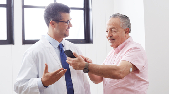 A FreeStyle Libre System Healthcare Professional and a FreeStyle Libre System user talking and smiling, while a FSL sensor is visible on the back of the user's arm.