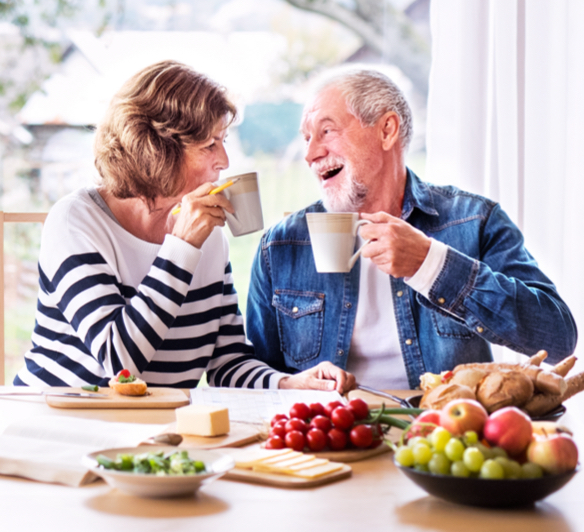 A woman and a man with mugs in their hands sitting at the table full of food.