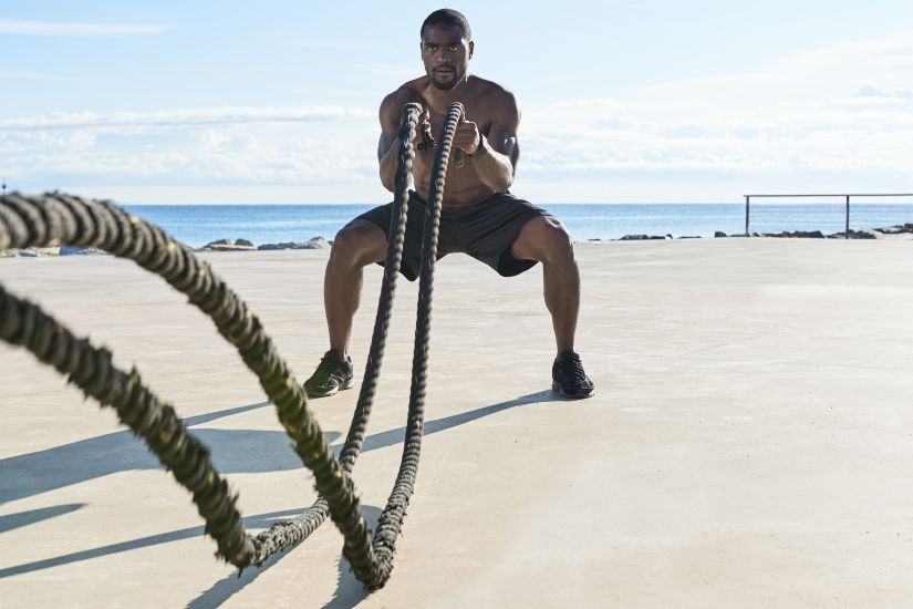 Homme puissant qui fait du sport avec des cordes épaisses sur la plage