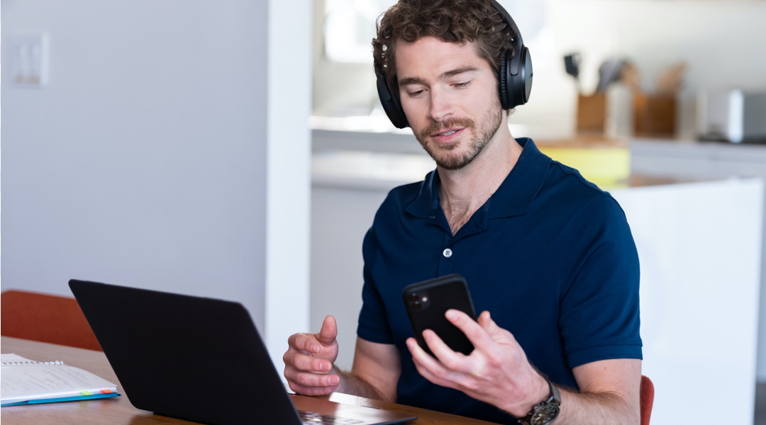 Man sitting in front of a desk wearing headphones and checking is phone