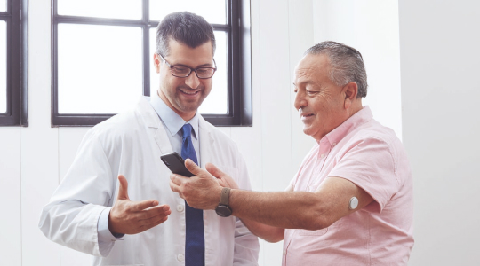 A FreeStyle Libre System user and Healthcare Professional sitting at the table applying the sensor on user's arm.
