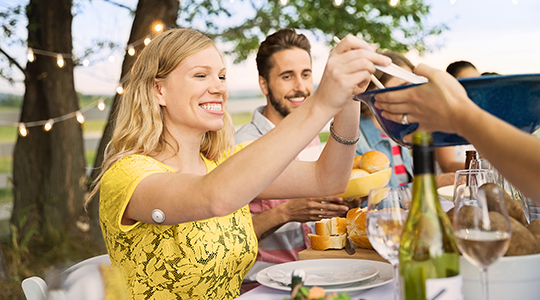 A woman eating outside in a gathering and smiling.