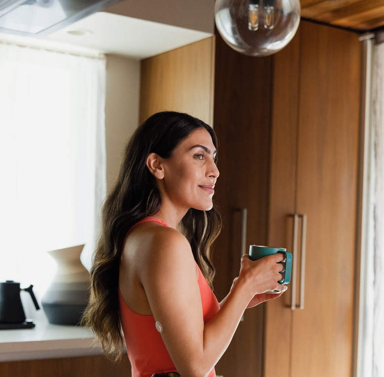 Vrouw die thee drinkt met FreeStyle Libre 3 Plus-sensor op arm