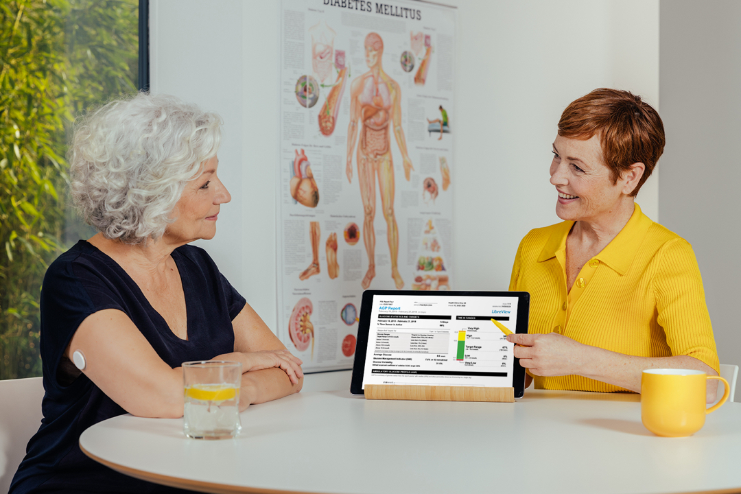 A FreeStyle Libre System user and Healthcare Professional sitting at the table talking about user's AGP Report. 