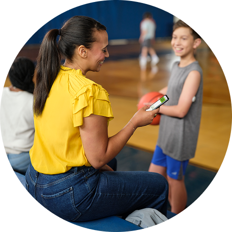 Woman looking at her phone and watching her son play basketball