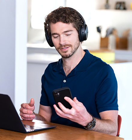 A man sitting in front of a laptop and checking his smartphone.