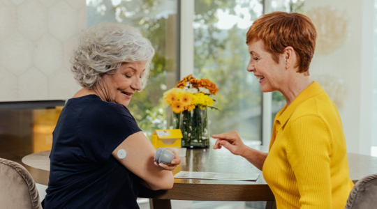 A FreeStyle Libre System user and Healthcare Professional sitting at the table applying the sensor on user's arm.