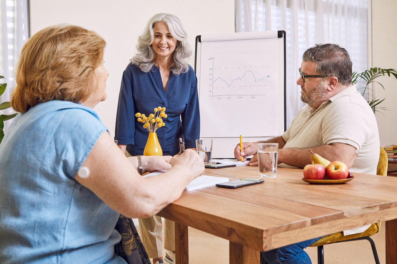 A FreeStyle Libre System Healthcare Professional and a FreeStyle Libre System user talking and smiling, while a FSL sensor is visible on the back of the user's arm.